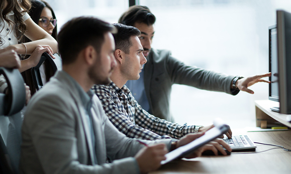 three men at desk looking at computer monitor